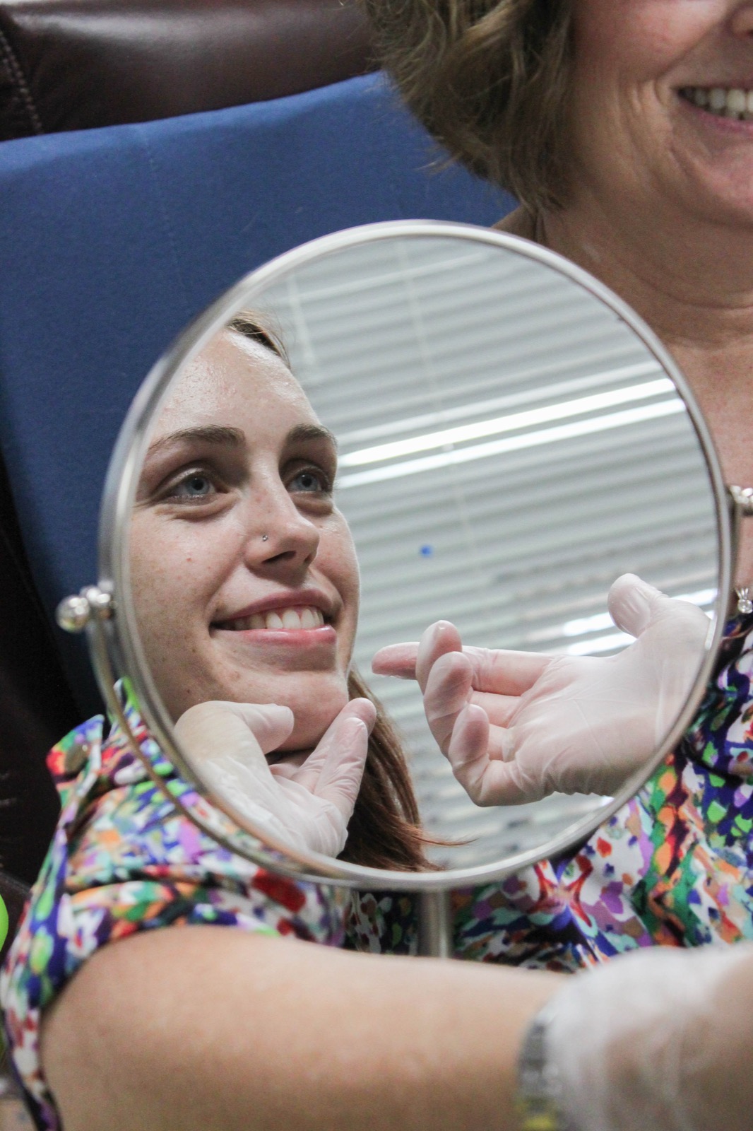 A patient smiling at a hand mirror during a tongue and jaw exercise